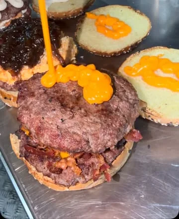 Hambúrgueres na chapa recebendo molho de queijo